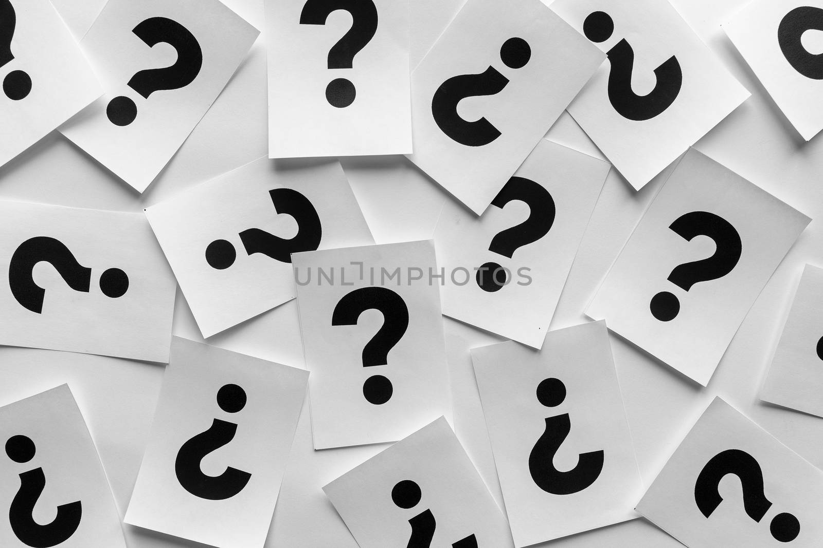 Bold black question marks on paper cards scattered randomly over a white background in a conceptual image