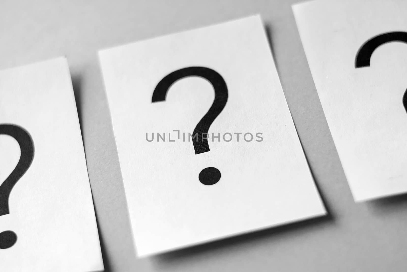 Row of black question marks printed on white sheets of paper viewed in close-up on grey background