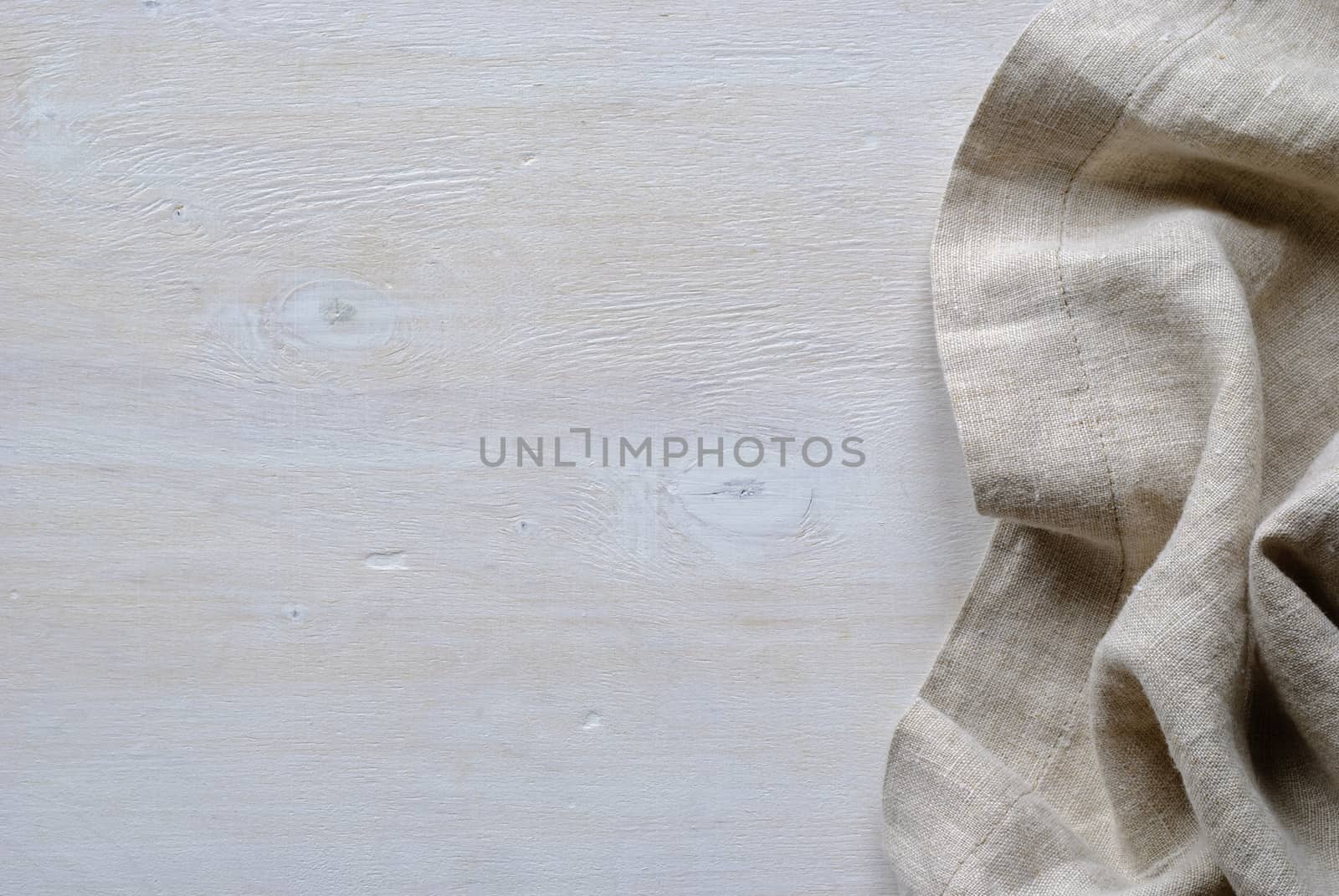 Folded and gathered linen fabric side border in a neutral weave over textured white painted wood with copy space