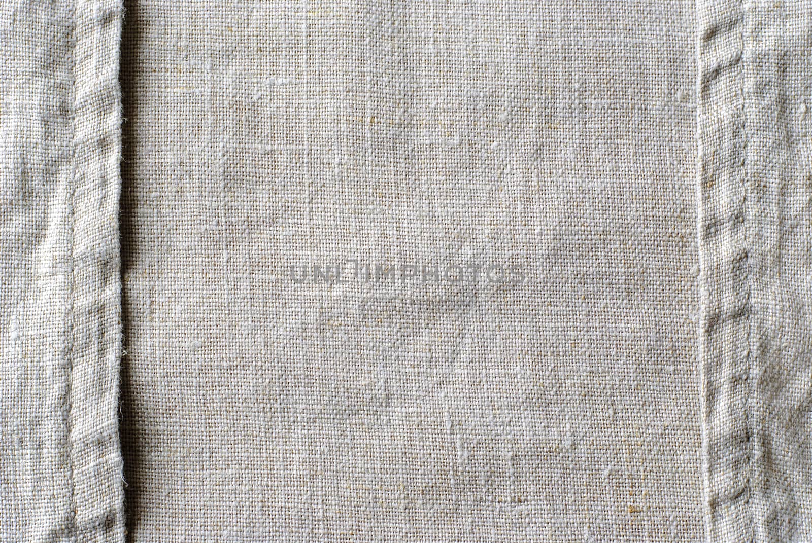 Stitched seams or edges on natural linen textile arranged as two borders to the sides over woven fabric centre with copy space