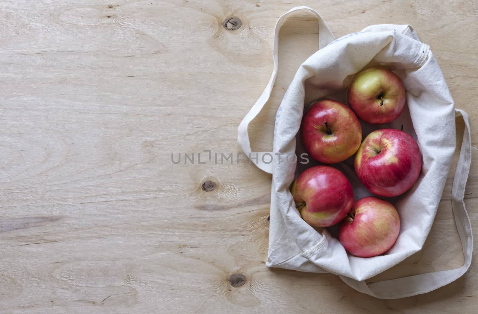 Fresh juicy apples displayed in a fabric bag on a wood panel background with copy space viewed from above