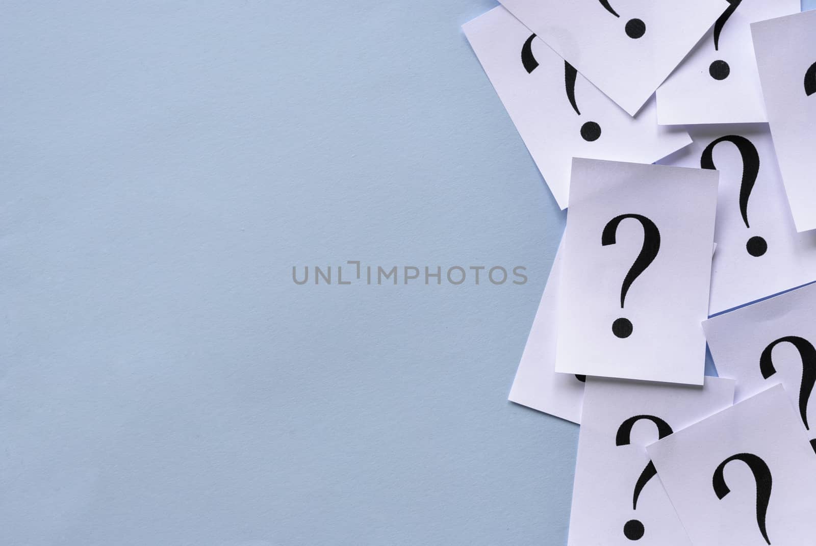 Side border of printed question marks on loose sheets of white paper overlaid together with lateral copy space on a blue background