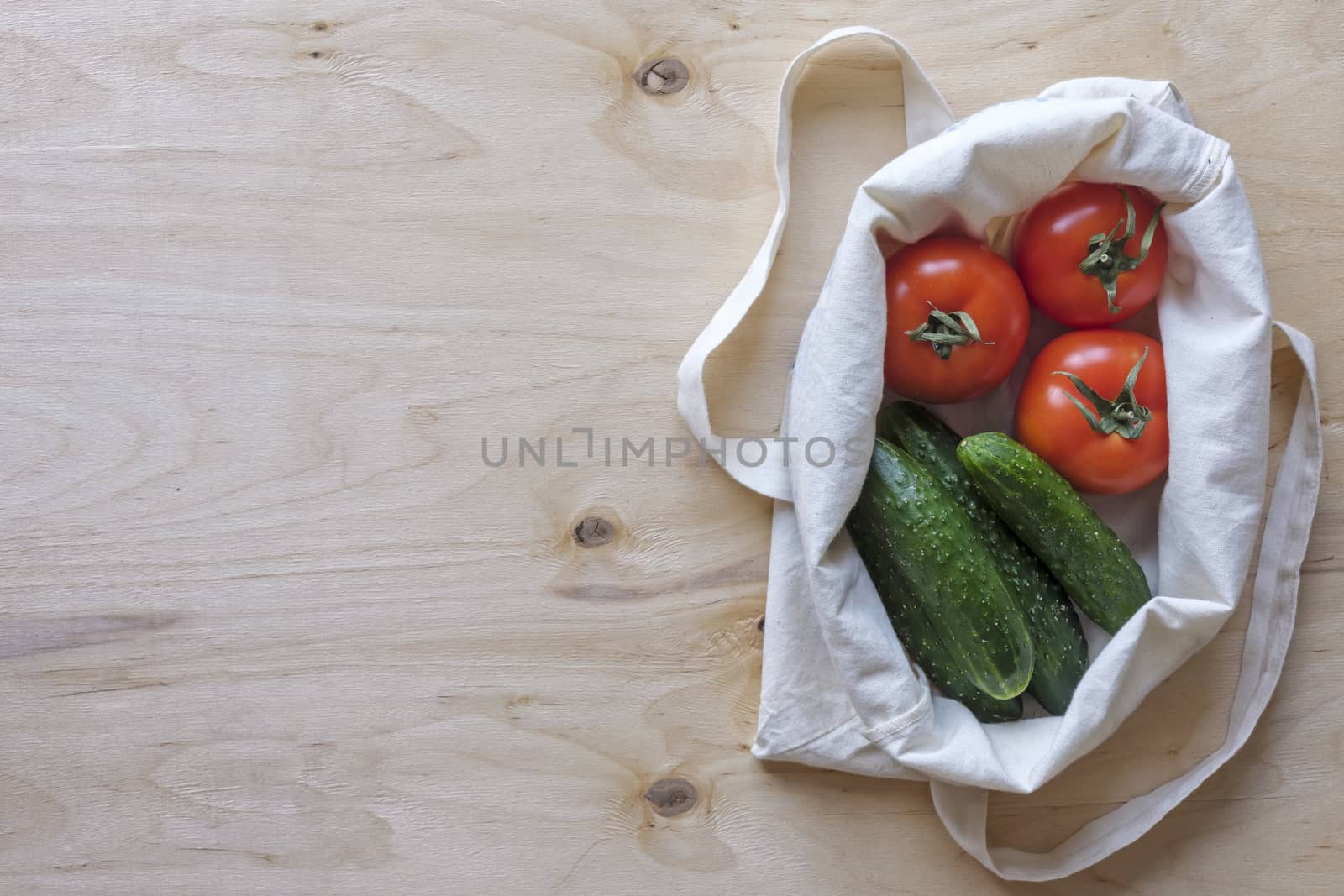 Fresh healthy salad tomatoes and cucumbers displayed in a cloth bag on a wood background with copy space