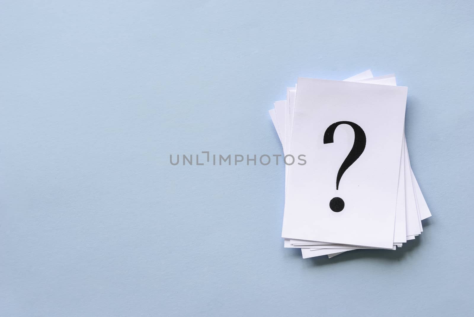 Pile of stacked question marks printed on sheets of white paper or signs arranged to the side on a blue background with copy space in a conceptual image