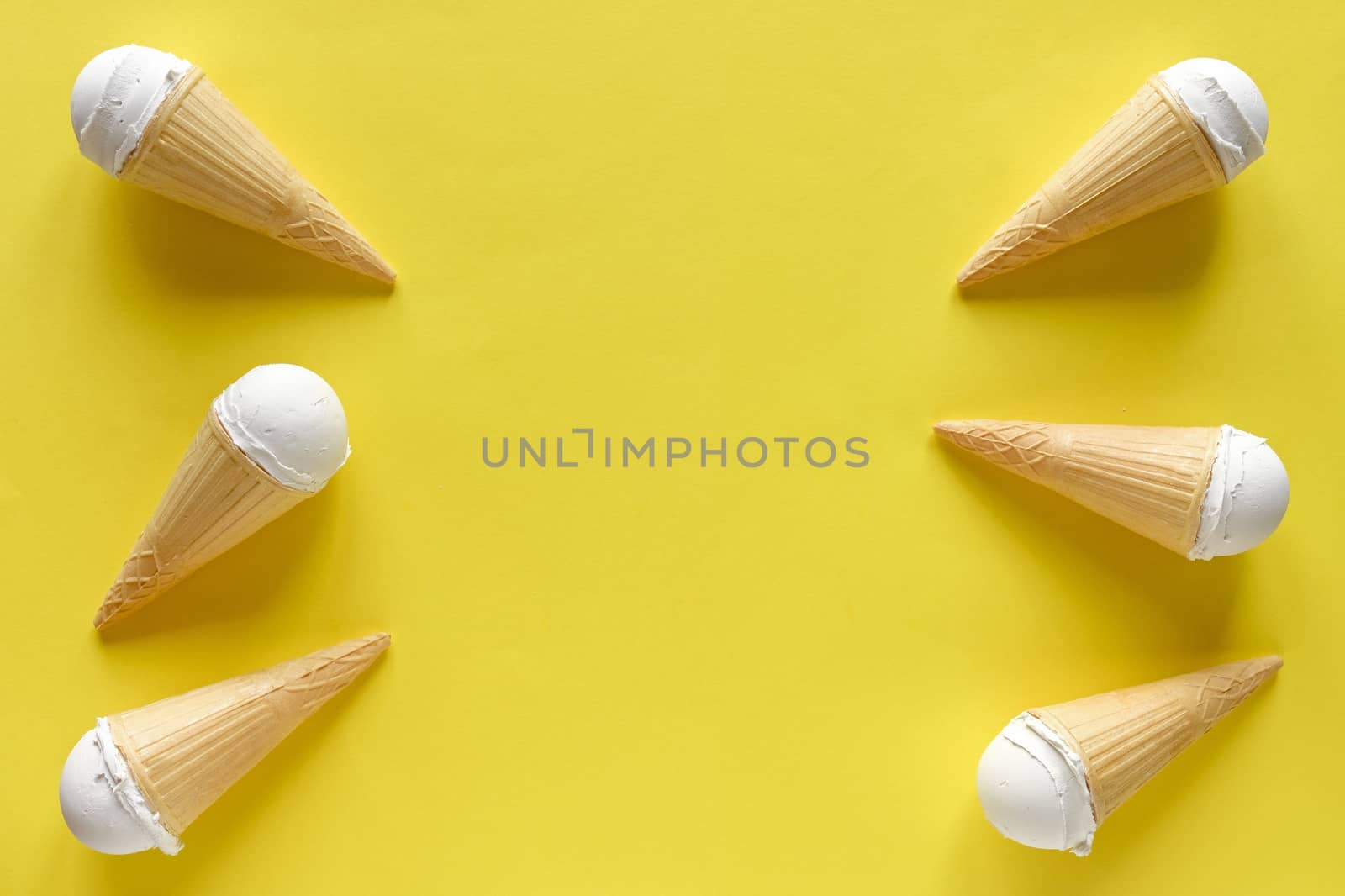 Double side border of vanilla ice cream cones on a colorful yellow background with central copy space for summer themed concepts