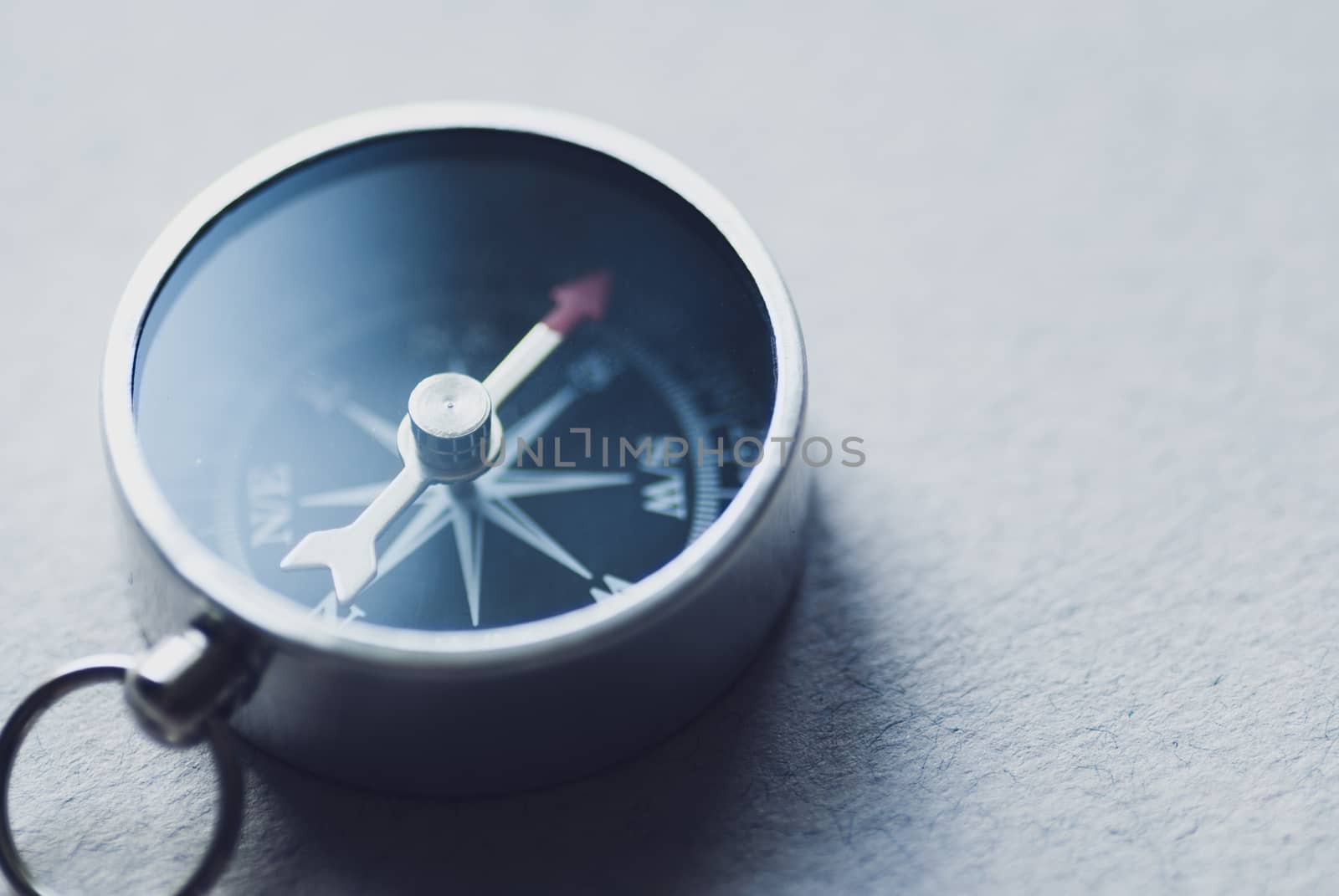 Small metallic magnetic compass on textured grey background for navigation or direction finding with lateral copy space