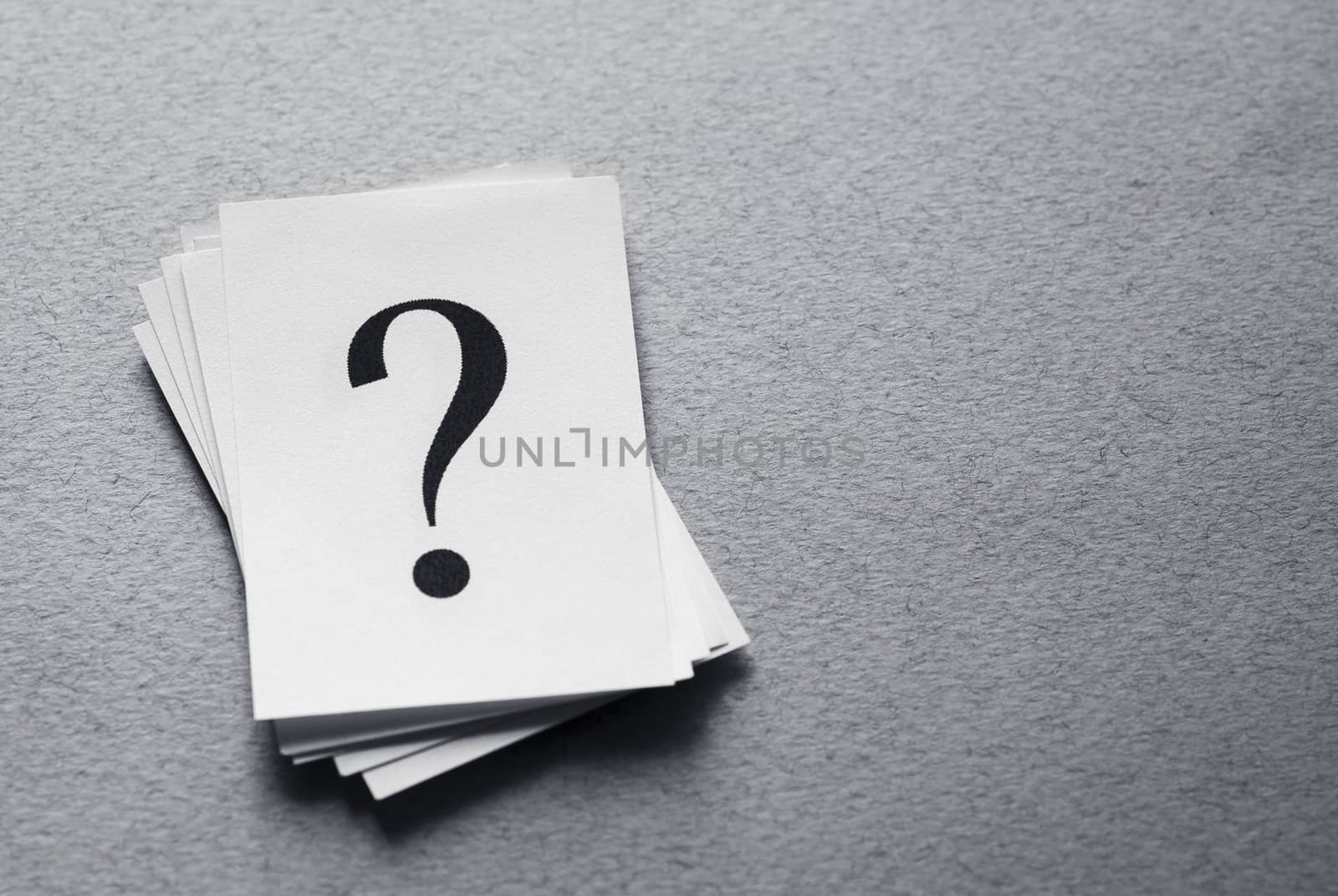 Pile of cards with printed question marks on a textured grey surface with copy space in a conceptual image