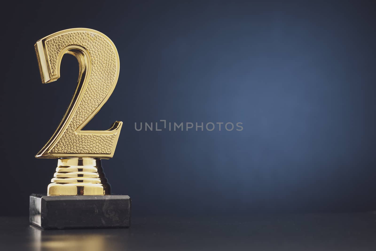 Second place winners gold trophy with a 3D textured metallic number two over blue with copy space