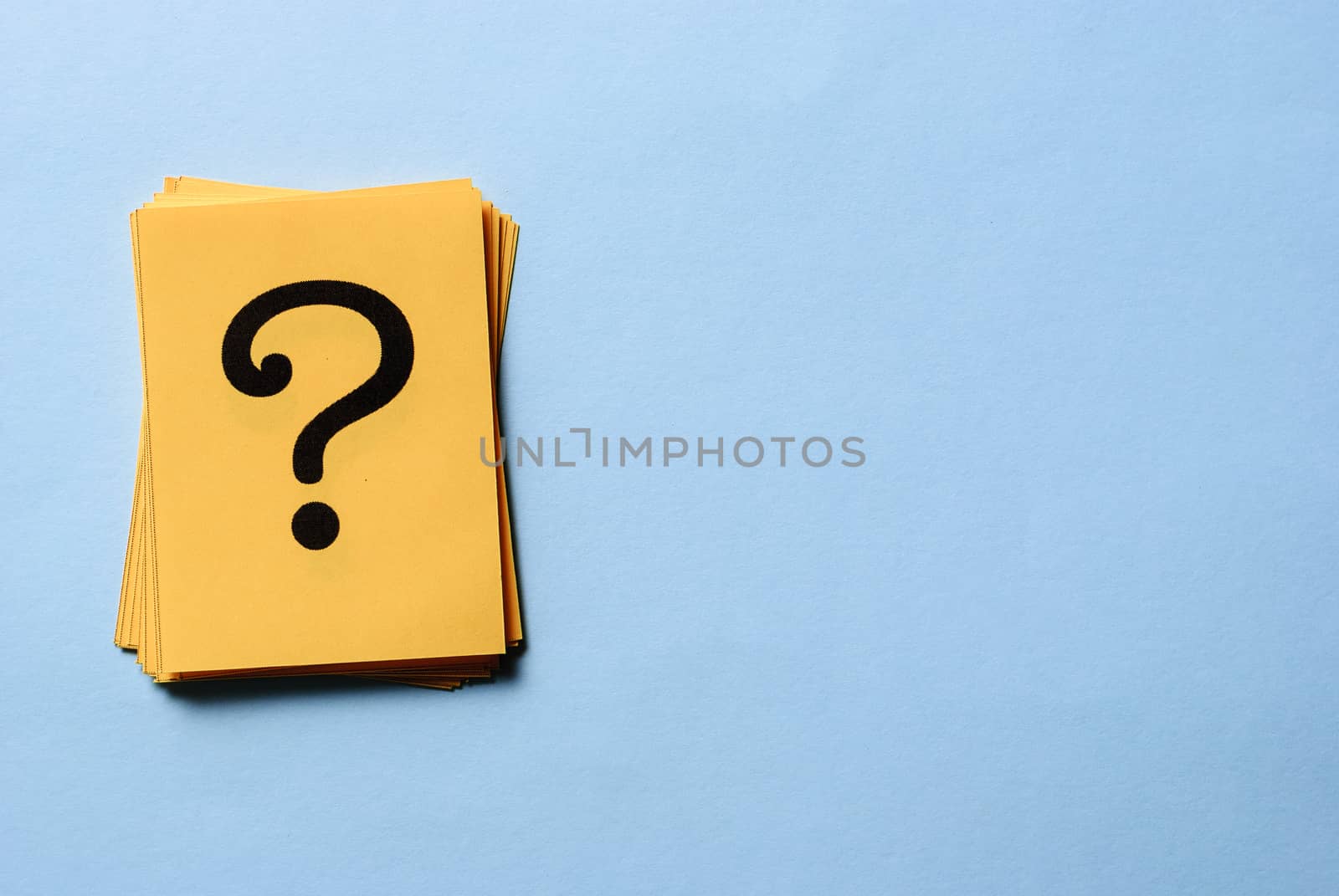 Stack of question marks on yellow cards arranged to the side on blue background with copy space