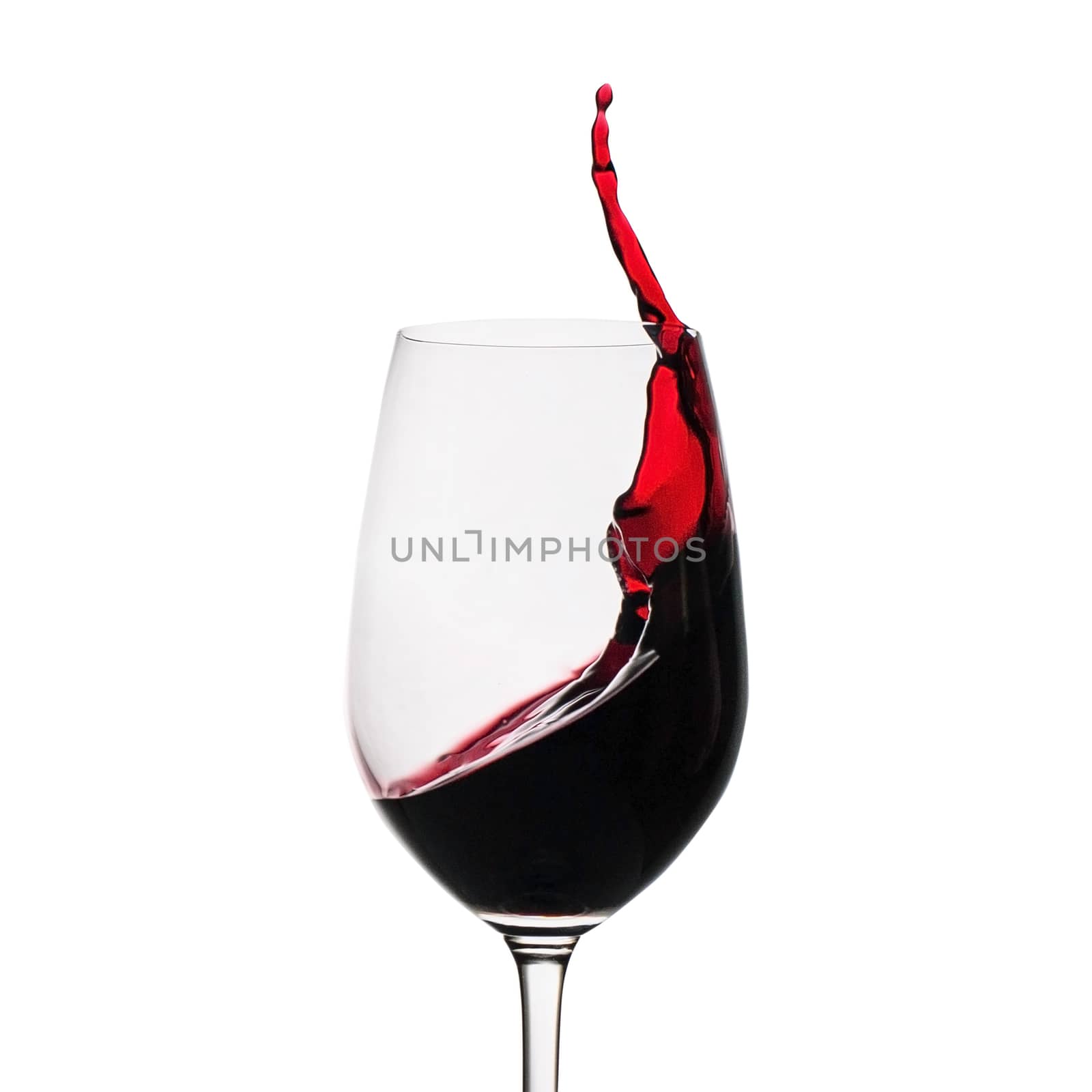 Freeze motion of red wine splashing up the side in a wineglass isolated on white with copy space