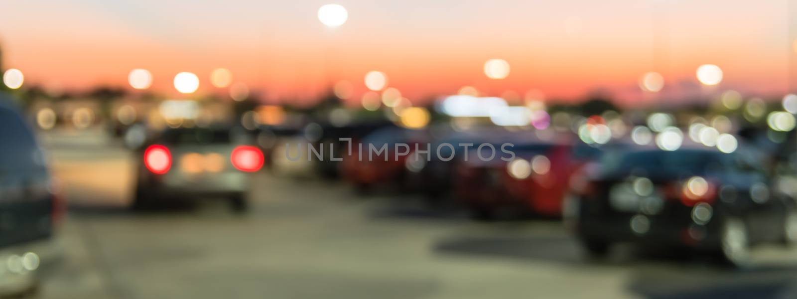 Panorama view abstract blurred parking lot of modern shopping center in Houston, Texas, USA. Exterior mall complex with row of cars in outdoor uncovered parking, bokeh light poles in background