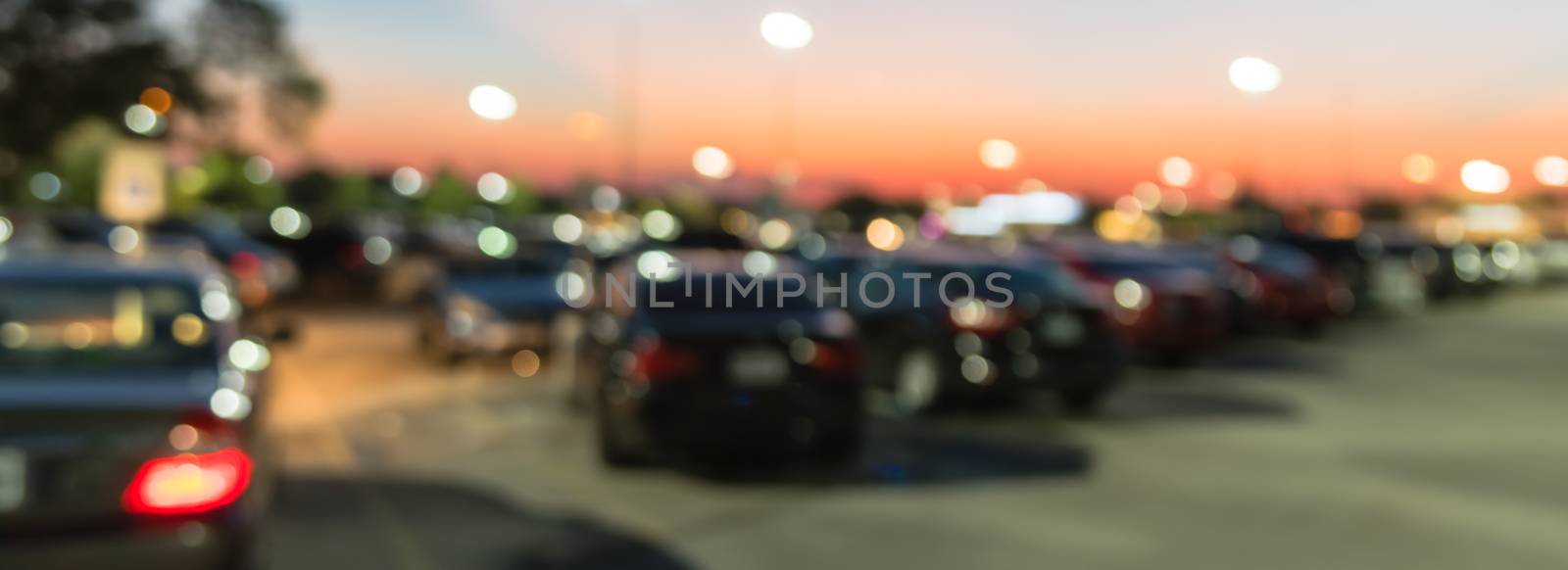 Panorama view abstract blurred parking lot of modern shopping center in Houston, Texas, USA. Exterior mall complex with row of cars in outdoor uncovered parking, bokeh light poles in background