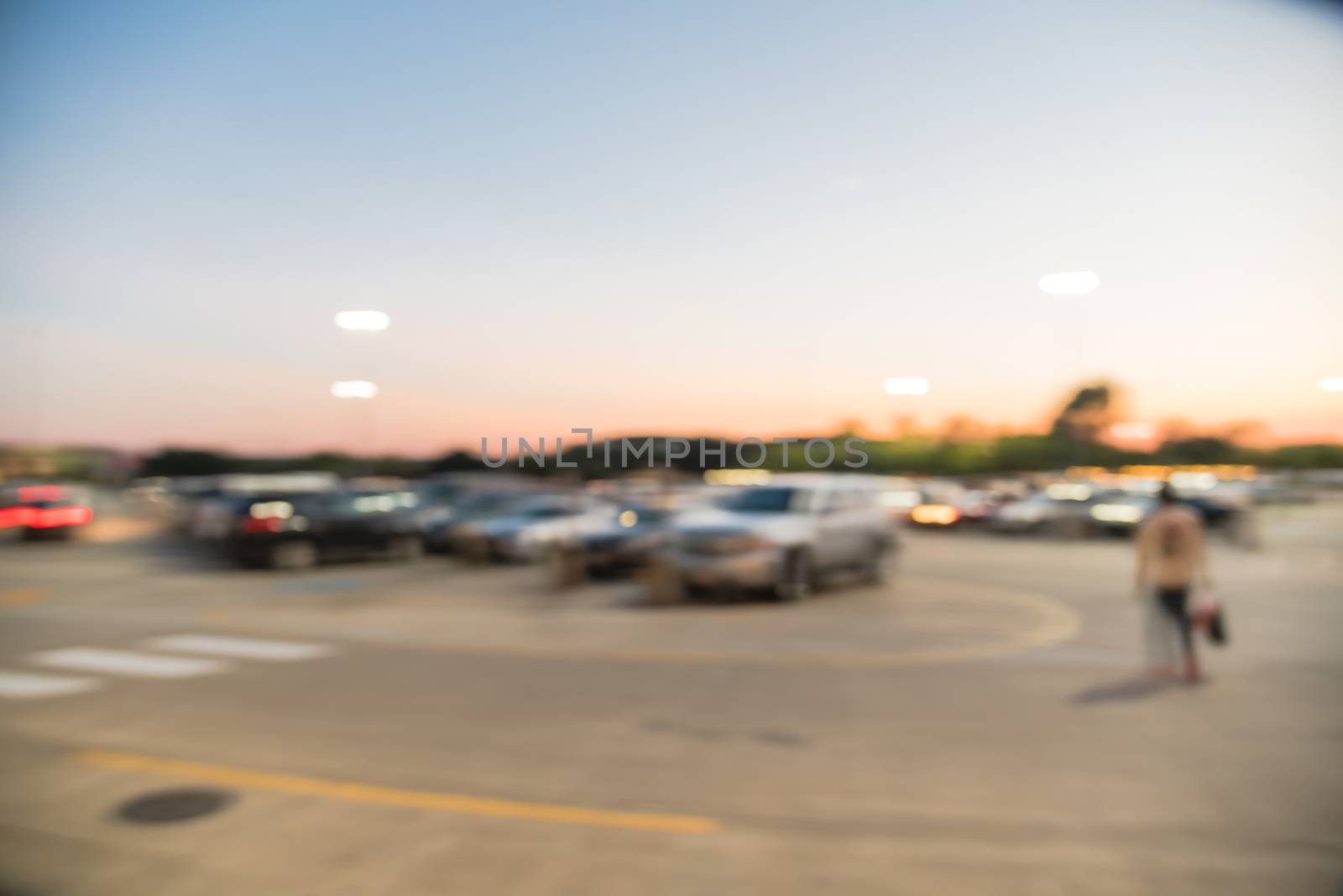 Motion blurred customer out shopping in holidays season at modern shopping center in Humble, Texas, US. Busy outdoor parking lots at sunset, mall complex uncovered parking with light lampposts