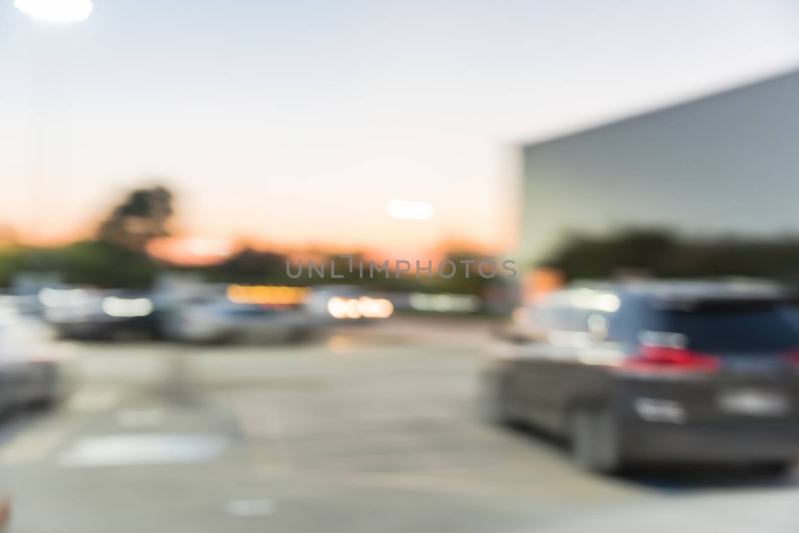 Blurred abstract retail store facade of modern shopping center in Humble, Texas, US at sunset. Mall complex with row of cars in outdoor uncovered parking lots with light poles in background