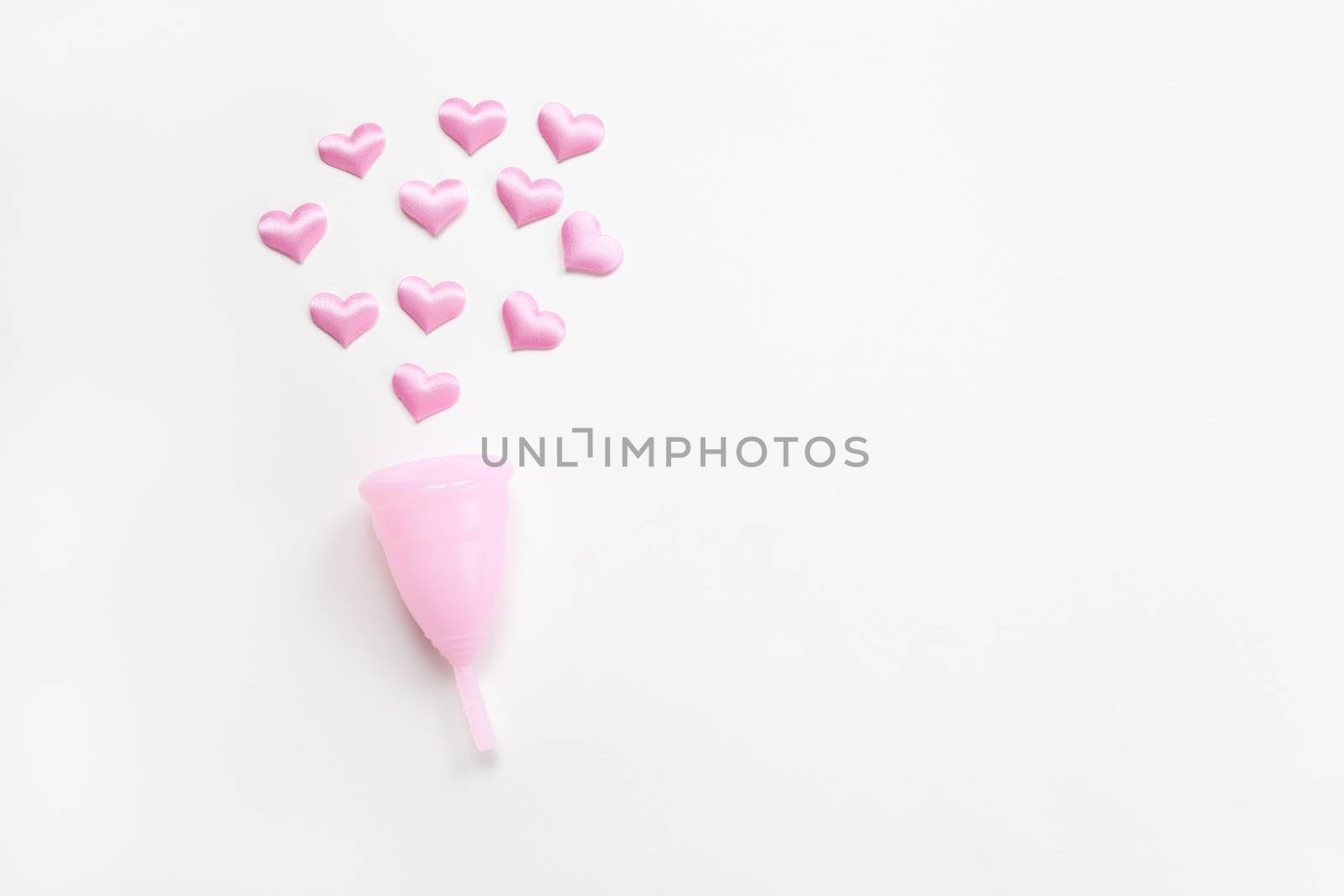 Pink menstrual cup on white background with small hearts. Concept zero waste, savings, environmental conservation, sustainable lifestyle. Feminine hygiene product, flatlay, copy space. Horizontal.