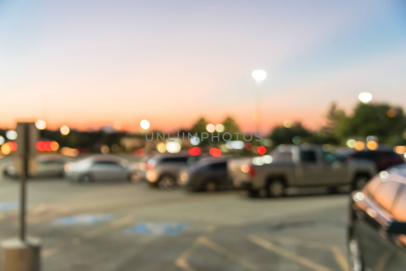 Abstract blurred parking lot of modern shopping center in Houston, Texas, USA. Exterior view mall complex with row of cars in outdoor uncovered parking, bokeh light poles in background