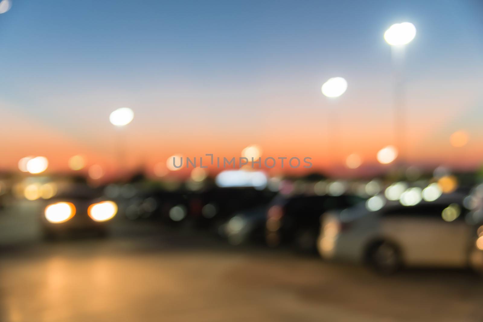 Abstract blurred parking lot of modern shopping center in Houston, Texas, USA. Exterior view mall complex with row of cars in outdoor uncovered parking, bokeh light poles in background