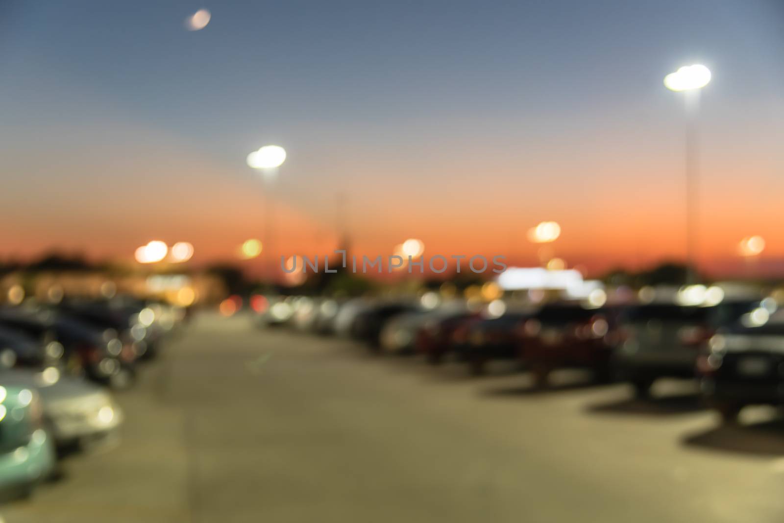 Abstract blurred parking lot of modern shopping center in Houston, Texas, USA. Exterior view mall complex with row of cars in outdoor uncovered parking, bokeh light poles in background