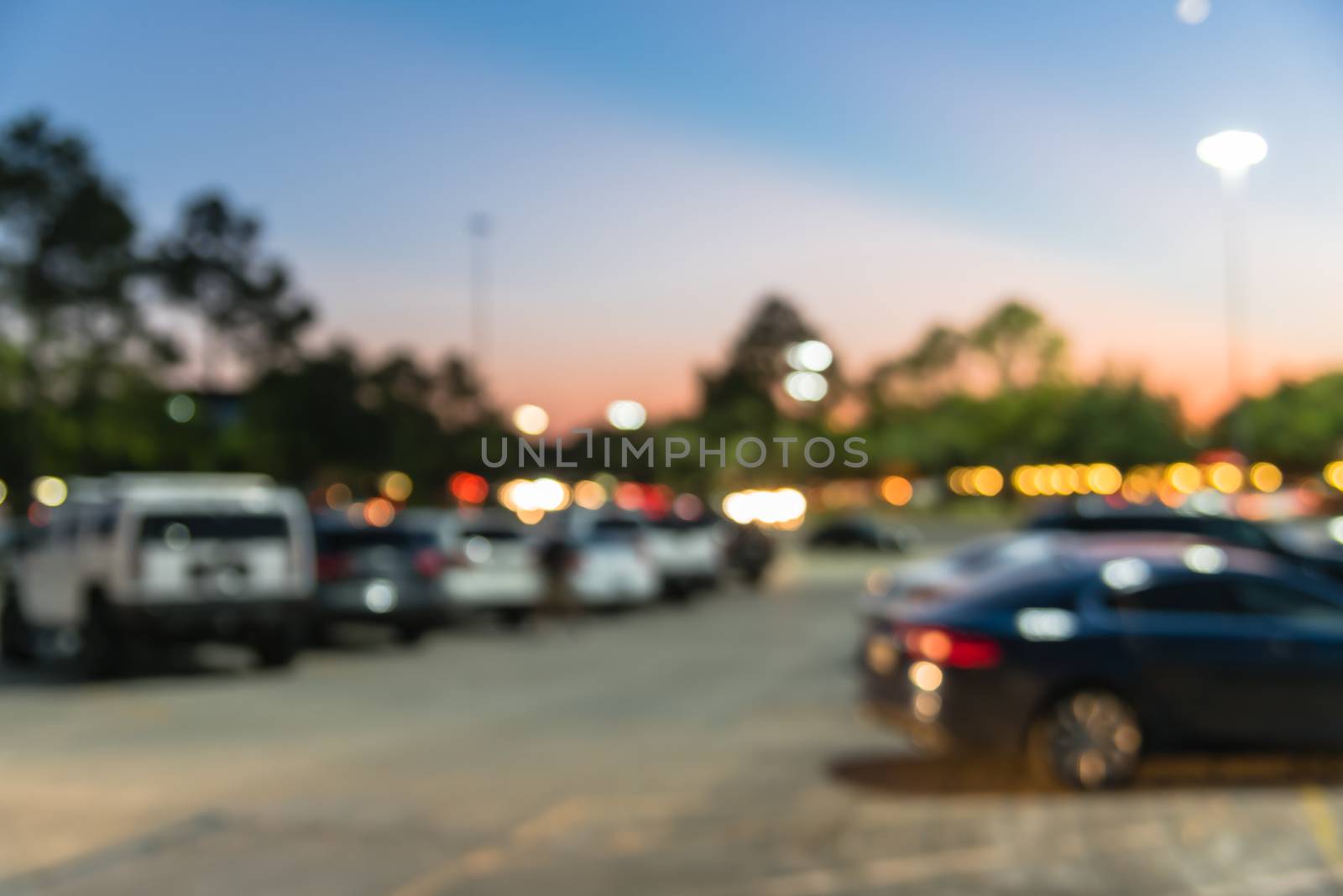 Blurred abstract retail store facade of modern shopping center in Humble, Texas, US at sunset. Mall complex with row of cars in outdoor uncovered parking lots with light poles in background