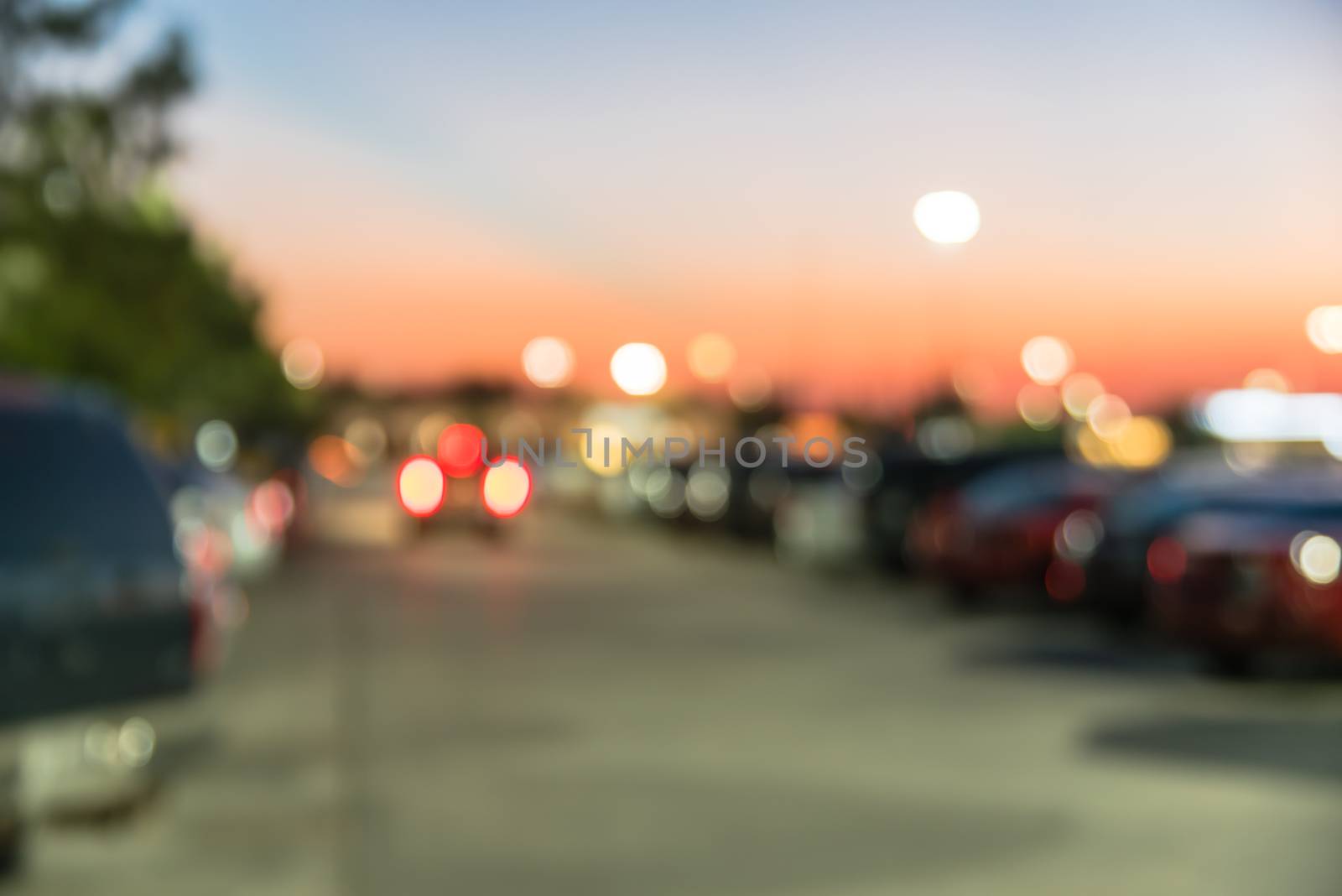 Blurred abstract retail store facade of modern shopping center in Humble, Texas, US at sunset. Mall complex with row of cars in outdoor uncovered parking lots with light poles in background