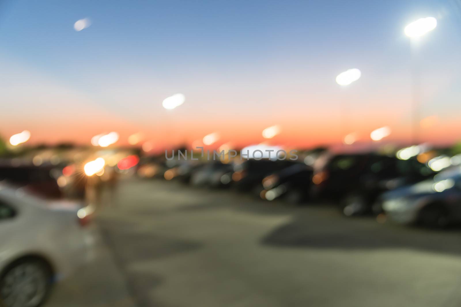 Abstract blurred parking lot of modern shopping center in Houston, Texas, USA. Exterior view mall complex with row of cars in outdoor uncovered parking, bokeh light poles in background