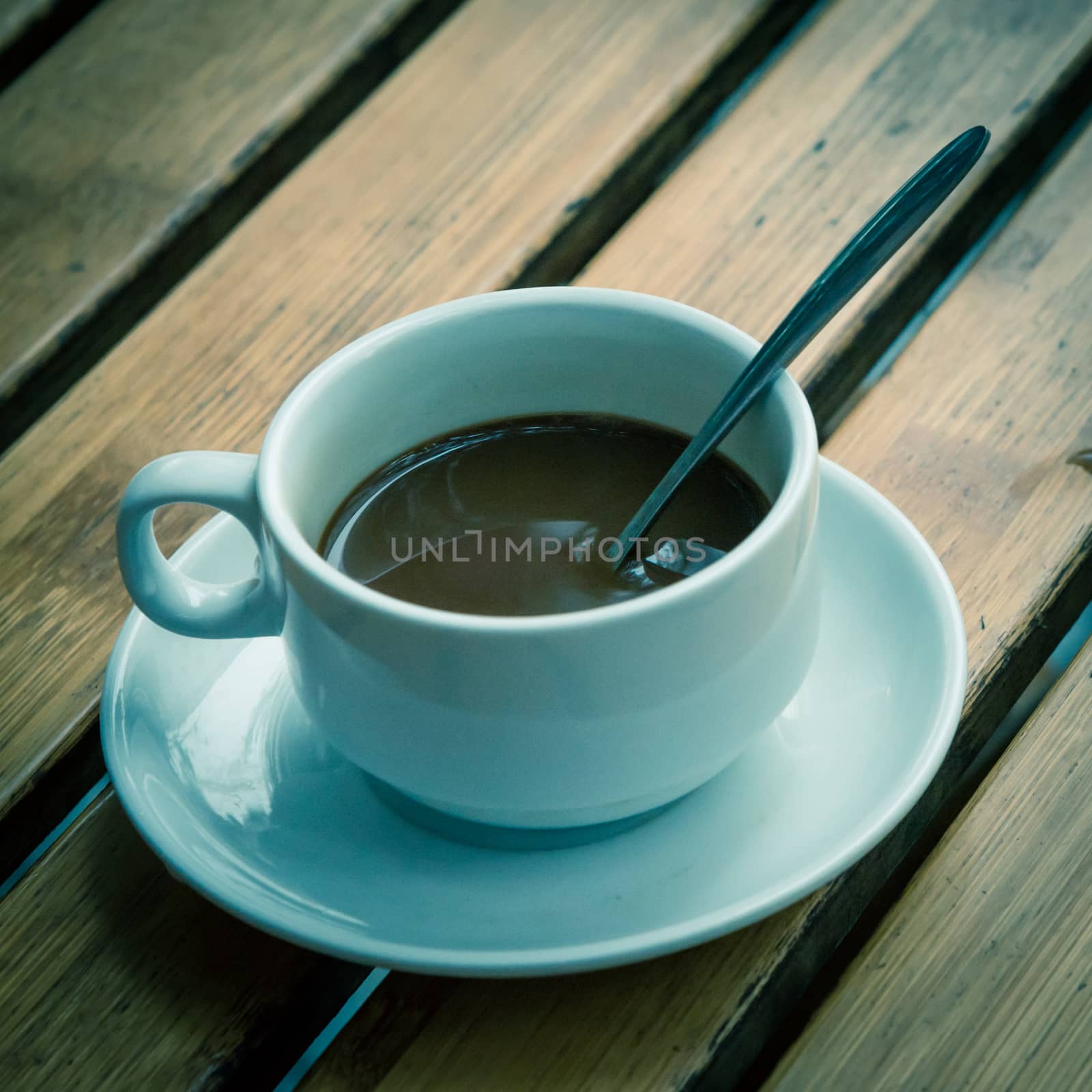 Toned photo of Popular Vietnamese milk coffee in ceramic cup and saucer with stainless spoon on outdoor wooden table. Top view a morning Vietnamese gourmet drink. Food concept.