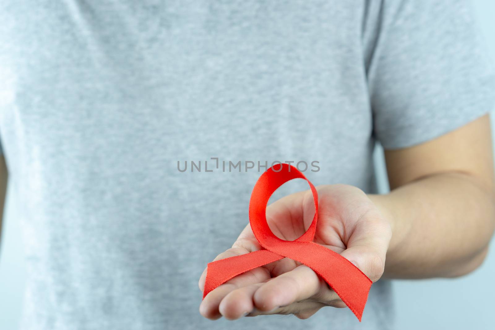 Aids awareness, male hands holding red AIDS awareness ribbon. World Aids Day, Healthcare and medical concept.