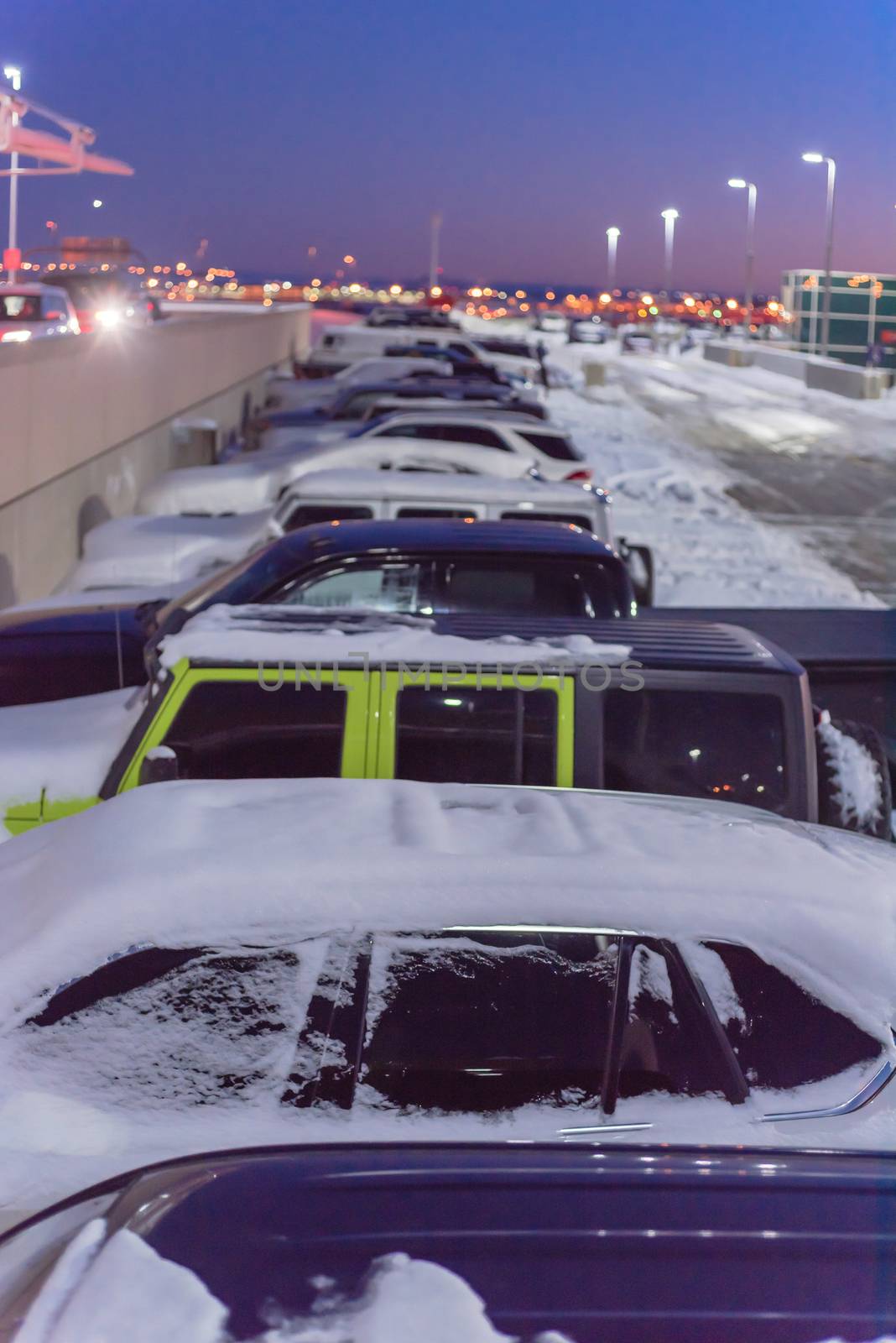 View from above row of cars at busy lot with snowdrifts during severe weather condition in Colorado, USA. Full terminal parking at Denver International Airport (DIA) in frosty cold autumn sunset