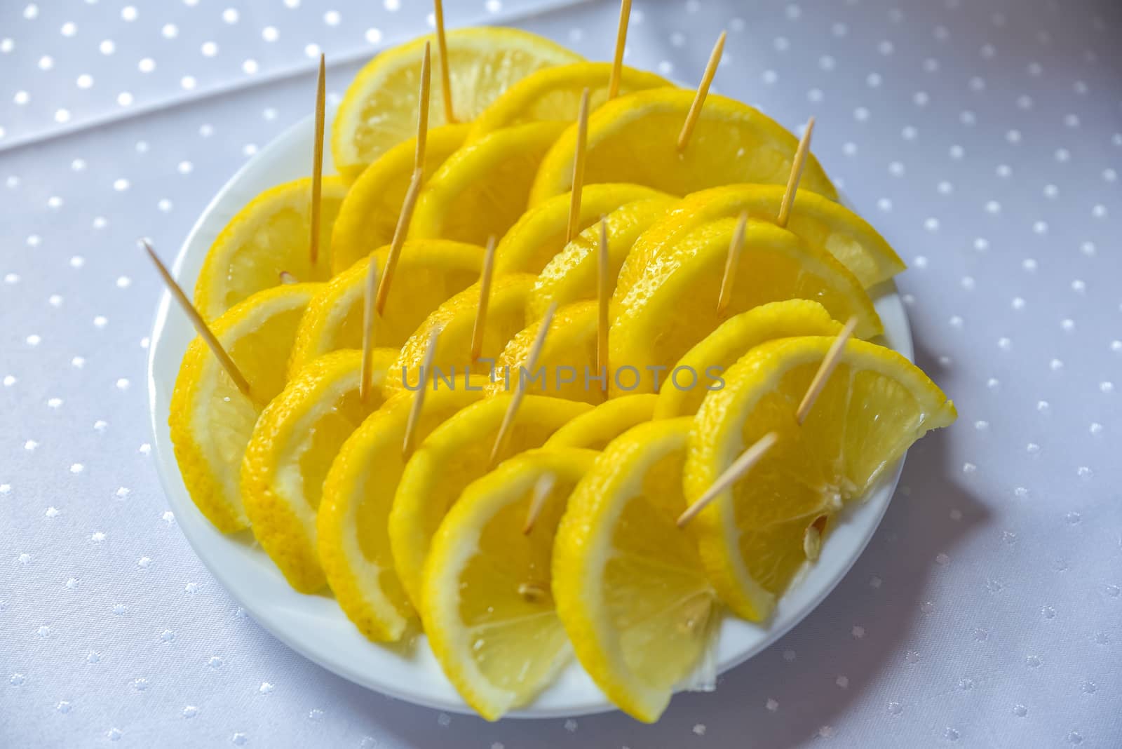 Yellow lemon slice standing on a white plat on blurred table