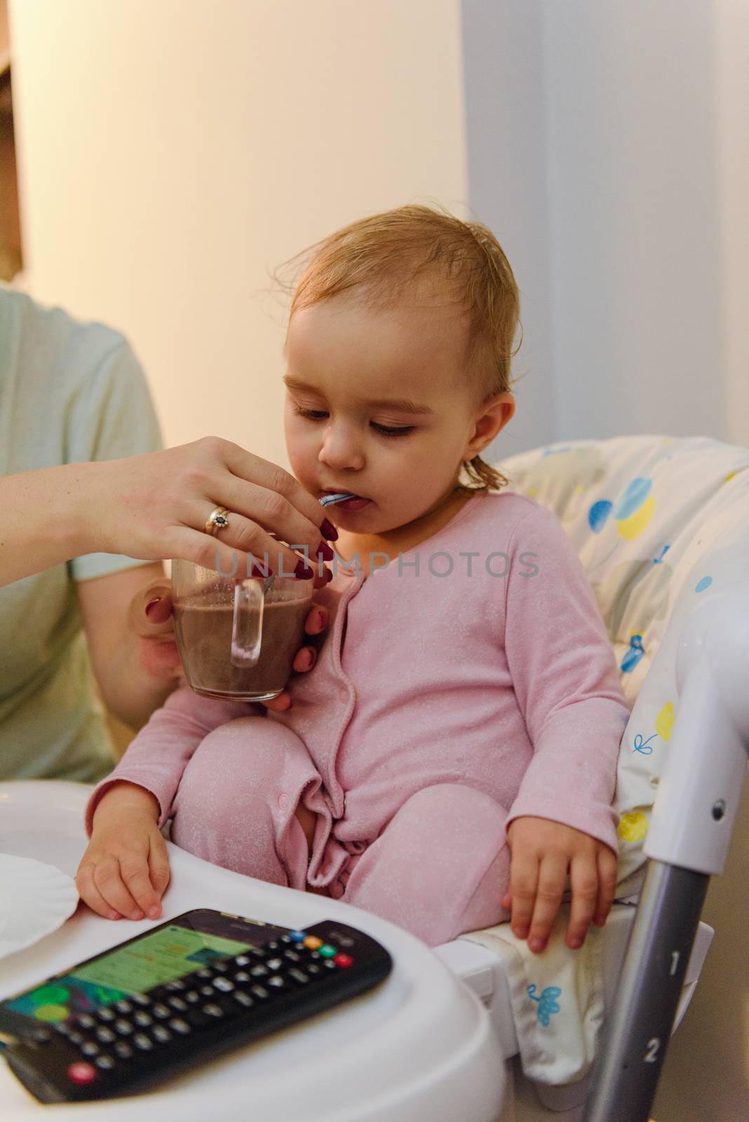cute blond child sits in a children's chair at the kitchen and eat a juicy peach. Little girl with a piercing look.