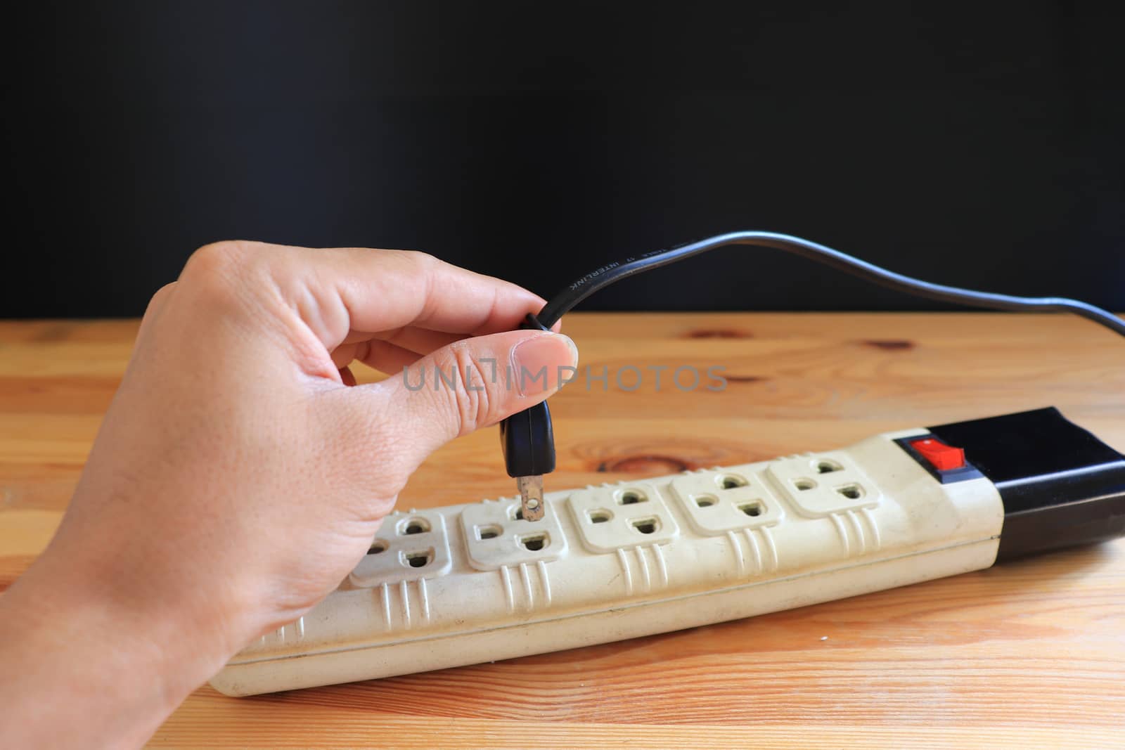 Hand holding electric plug,Electric Three eye plug on wooden background and black wall