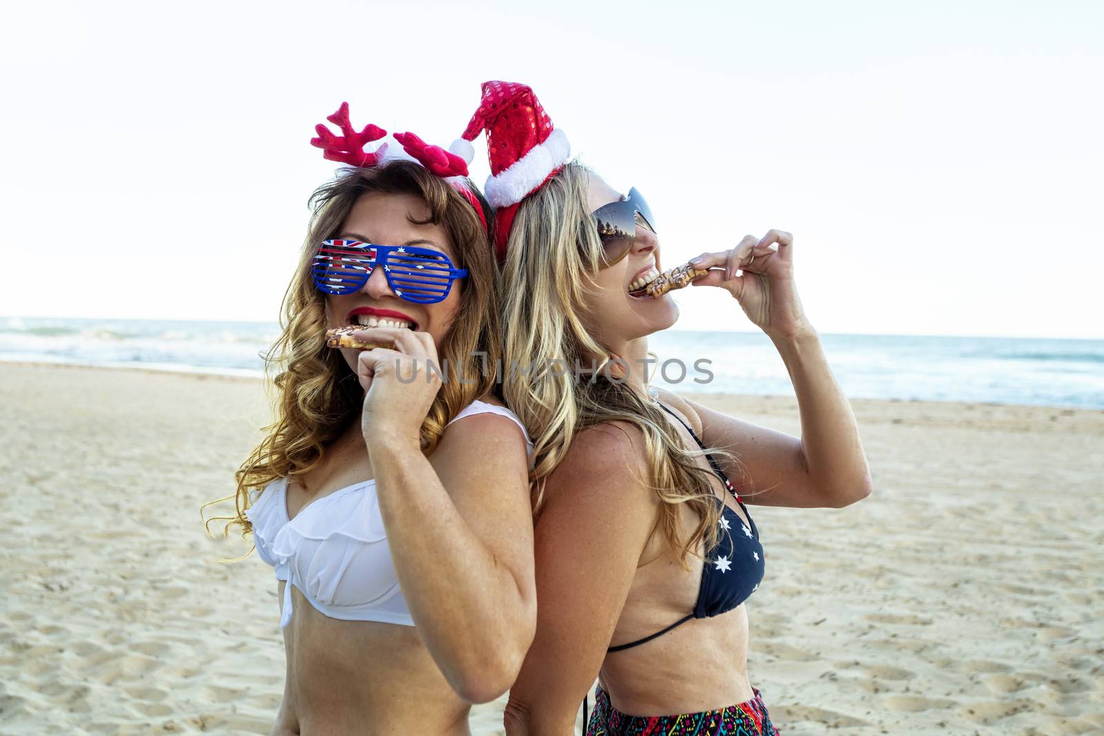 Two women eating festive food on the beach at Christmas by lovleah