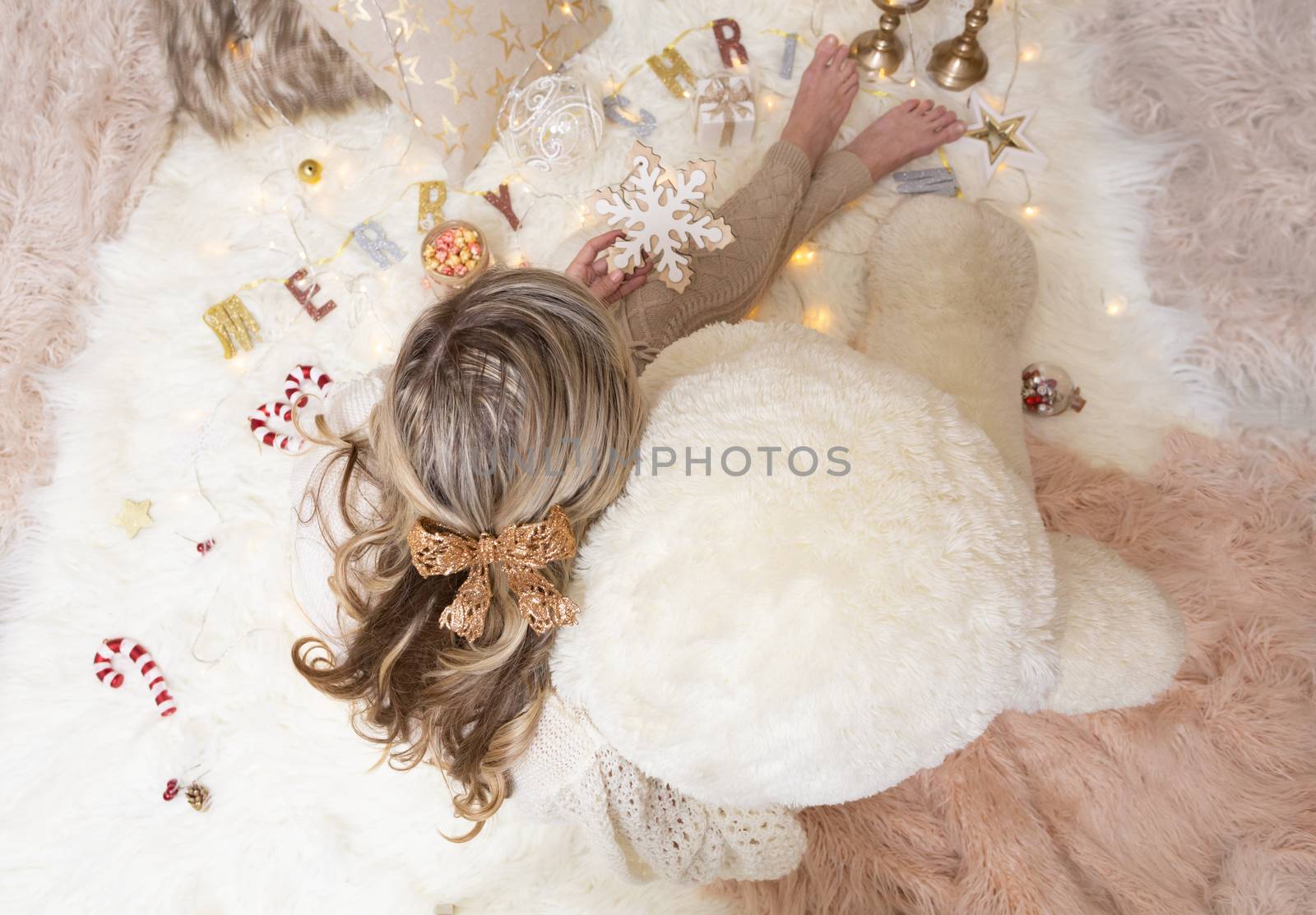 A woman sits among Christmas decorations.  She is holding a snowflake ornament for the Christmas tree