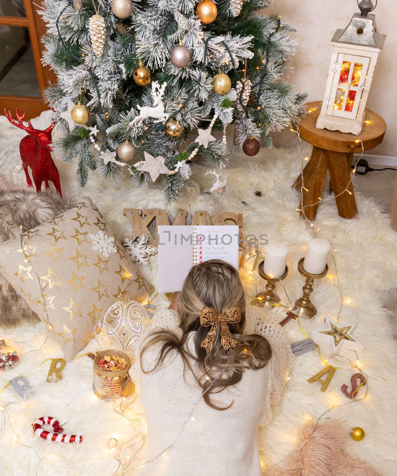 Woman makes her Christmas shopping list while lying in front of the Christmas tree with Chiristmas decorations all around her