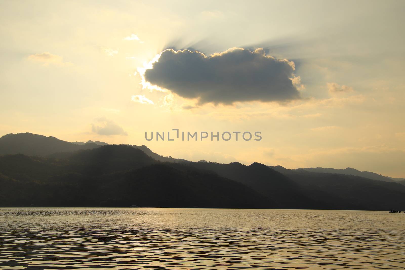 Lake in the evening With the sky and clouds and the mountains,tree on mountain,There is light behind the clouds.