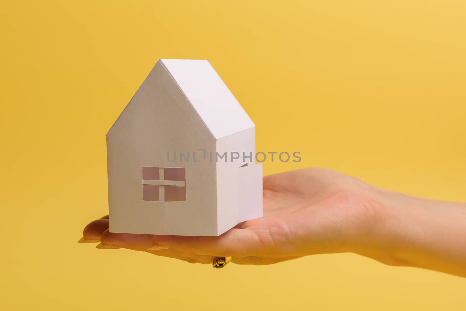 White family paper house in man hand on yellow background paper. Minimalistic style. Copy space. View from above. Vertical orientation