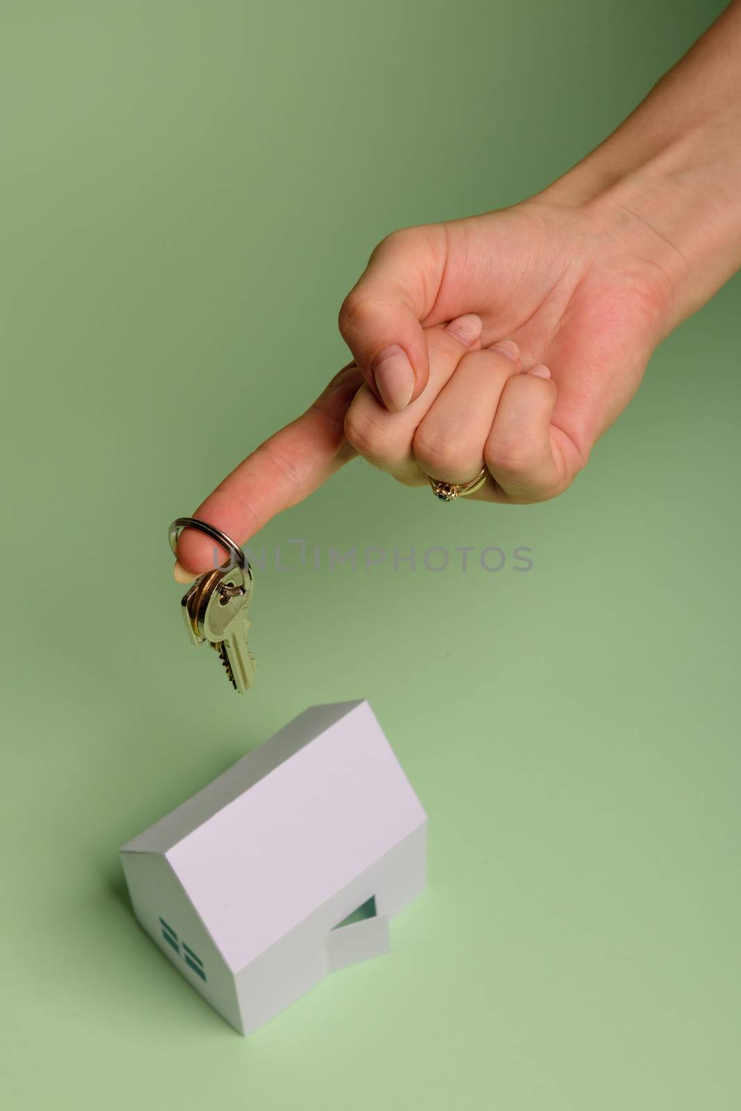 White family paper house. House keys in hand on mint background paper. Minimalistic and simple concept, style. Copy space. Vertical orientation. Family moving or removal concept.