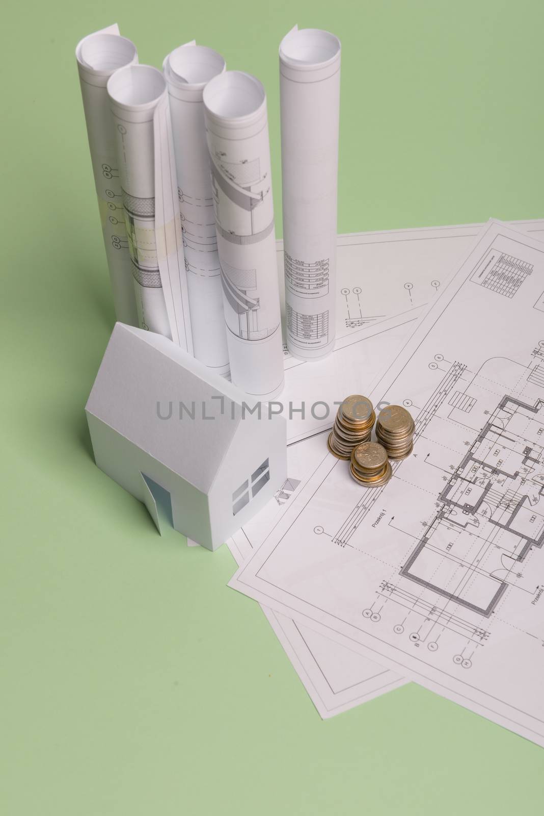 White family paper house , stack of money coins, house projects plan and blueprints on mint background paper. Minimalistic and simple concept, style. Vertical orientation