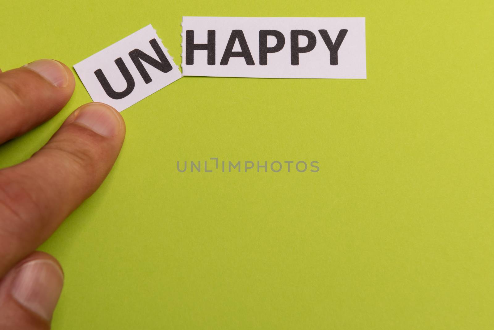 man hand holding card with text unhappy, cutting word 'un' so it written 'happy'. Copy space. Lime background. Studio shoot.