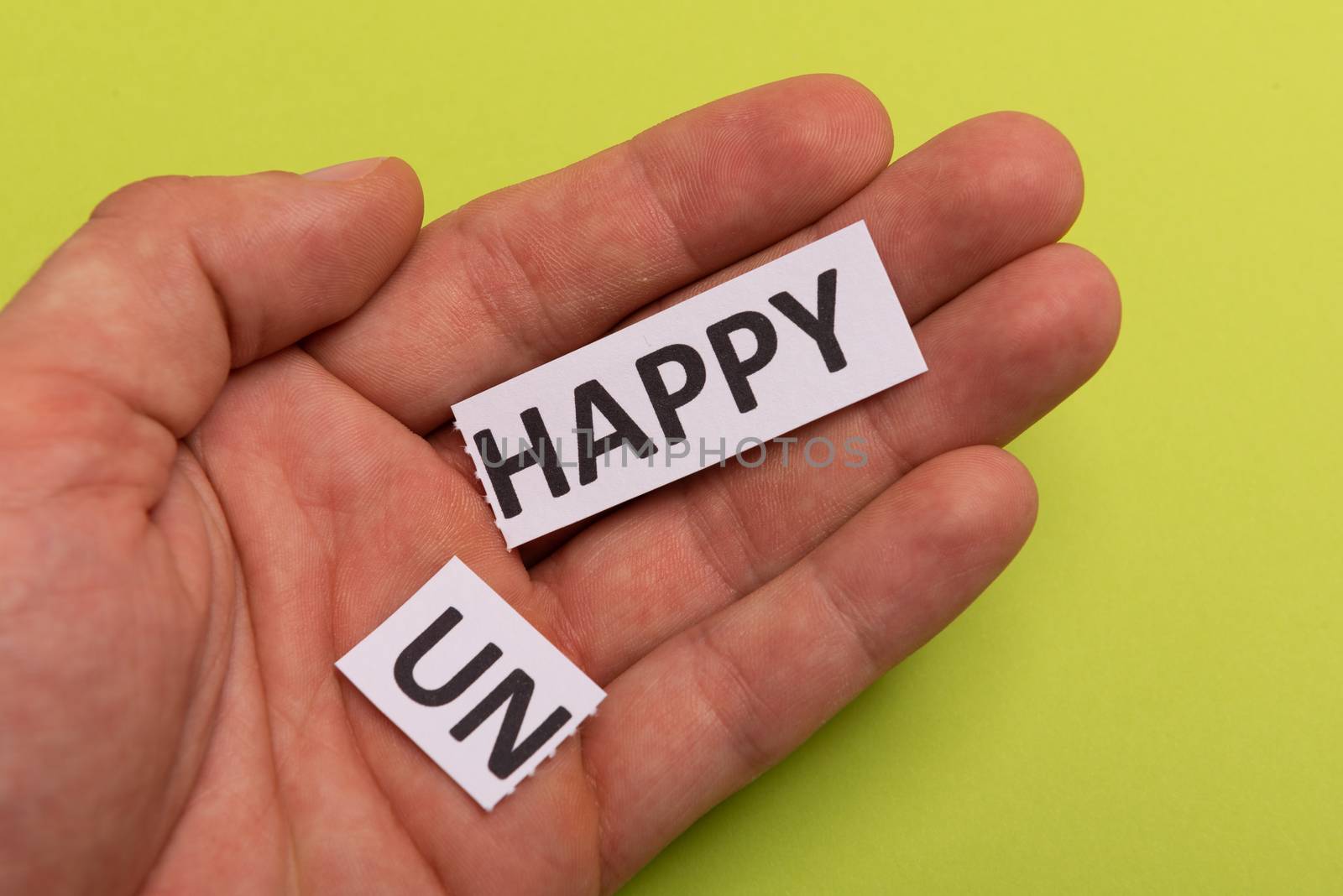 man hand holding card with text unhappy, cutting word 'un' so it written 'happy'. Copy space. Lime background. Studio shoot.