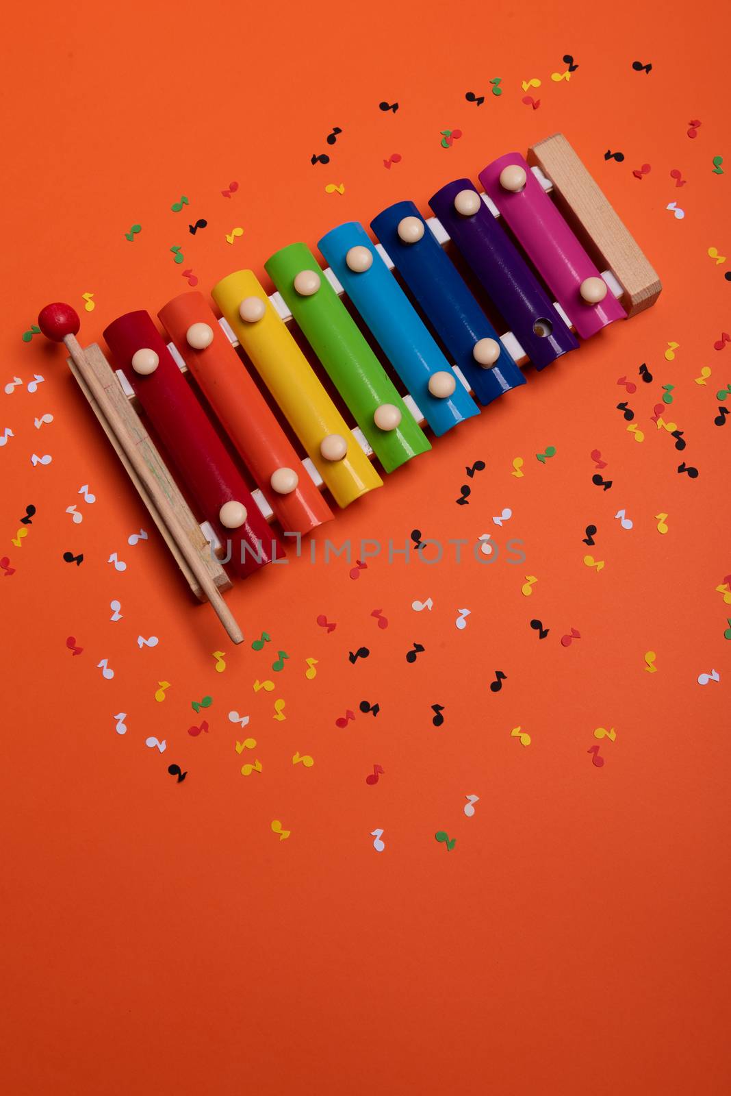 Wooden xylophone in rainbow colors for children an isolated on orange. Paper colorful musical notes surrounding .