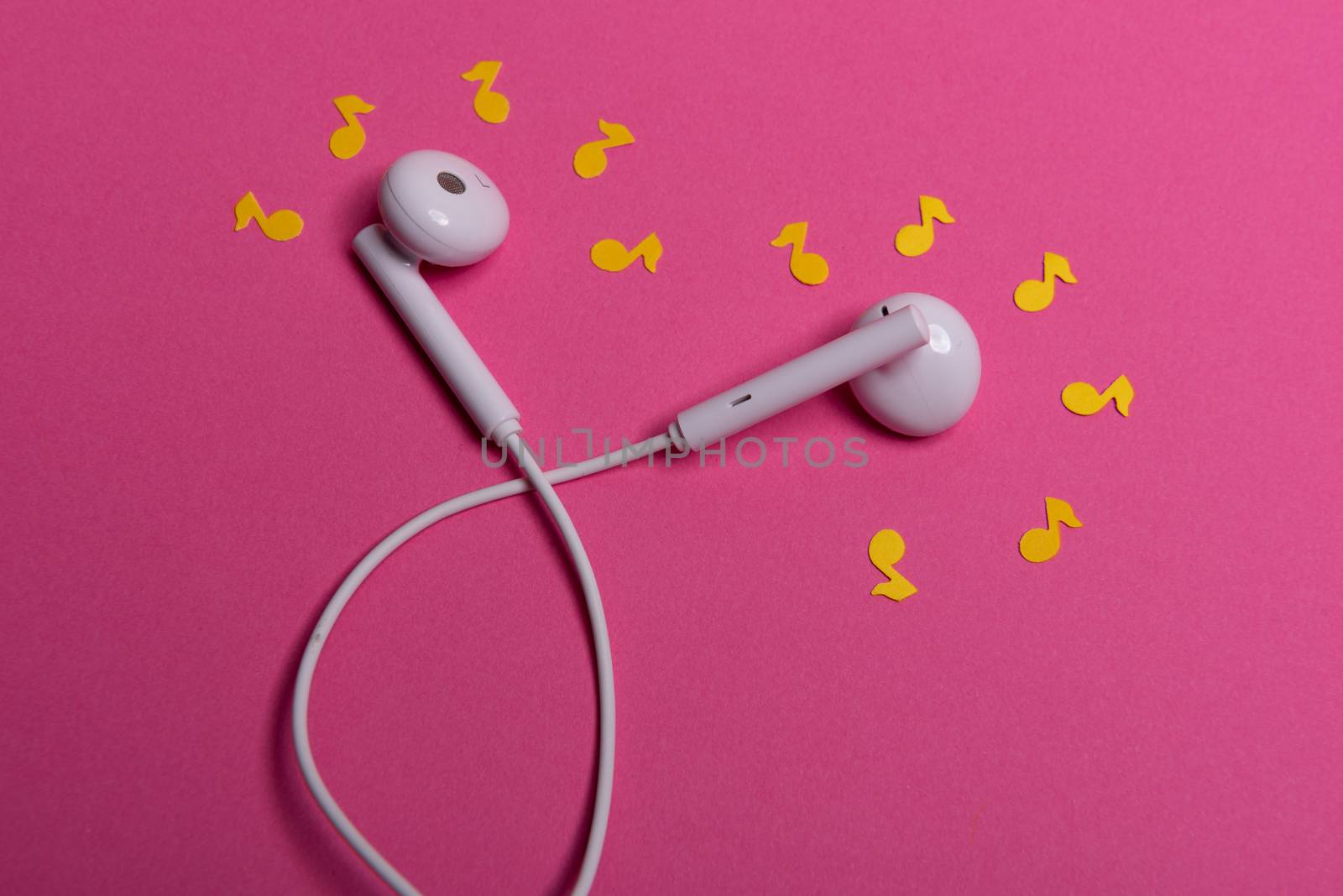 white earphones and yellow paper notes on pink background. view from above
