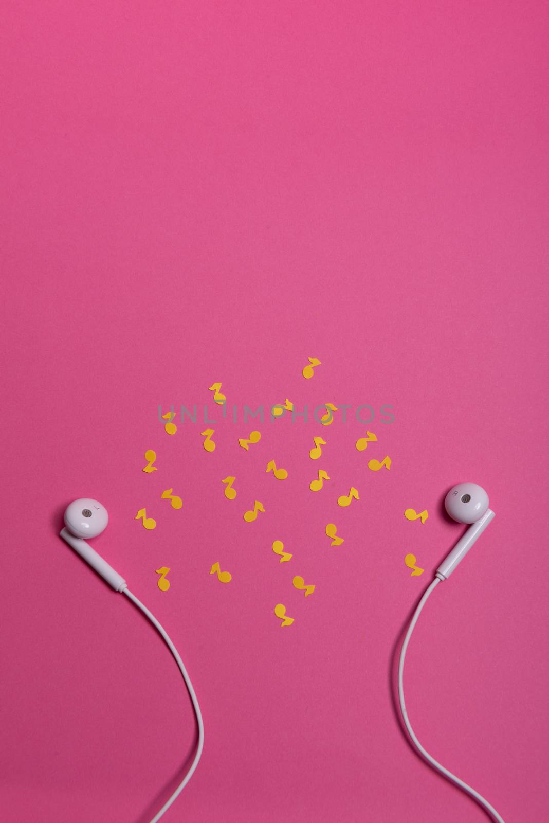 white earphones and yellow paper notes on pink background. view from above