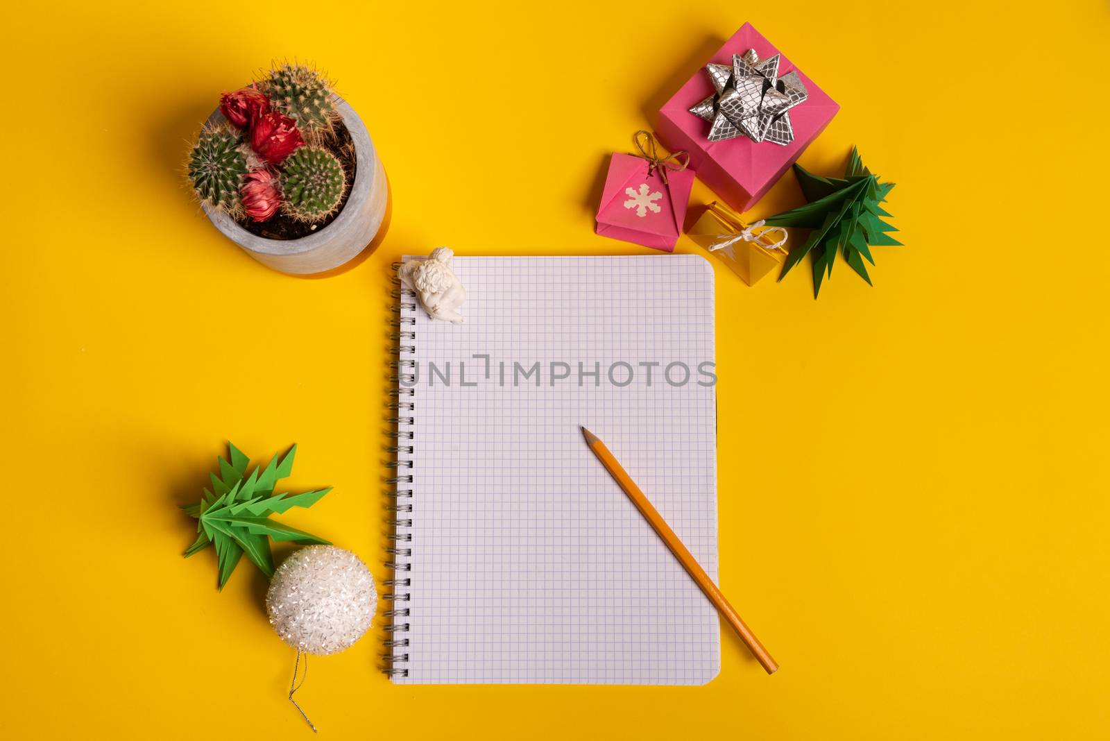 gift box and green origami trees with notepad on yellow desk, table