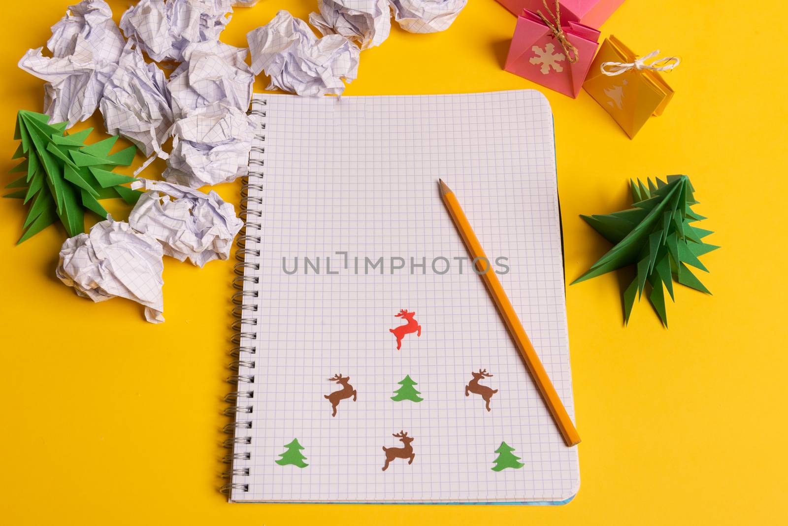 gift box and green paper origami trees with notepad on yellow desk, table. Christmas to do list text.