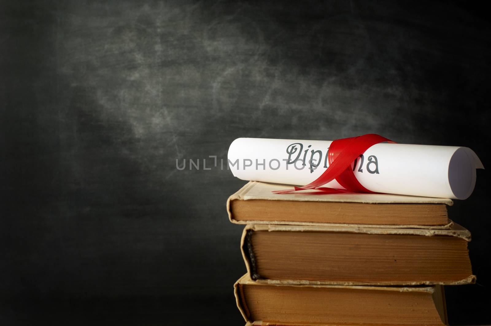 Diploma with red ribbon and stack of books against the background of blackboard