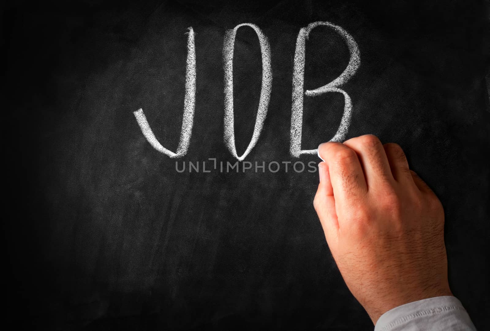 Male hand writing the word Job in capital letters on a black chalkboard with a piece of chalk
