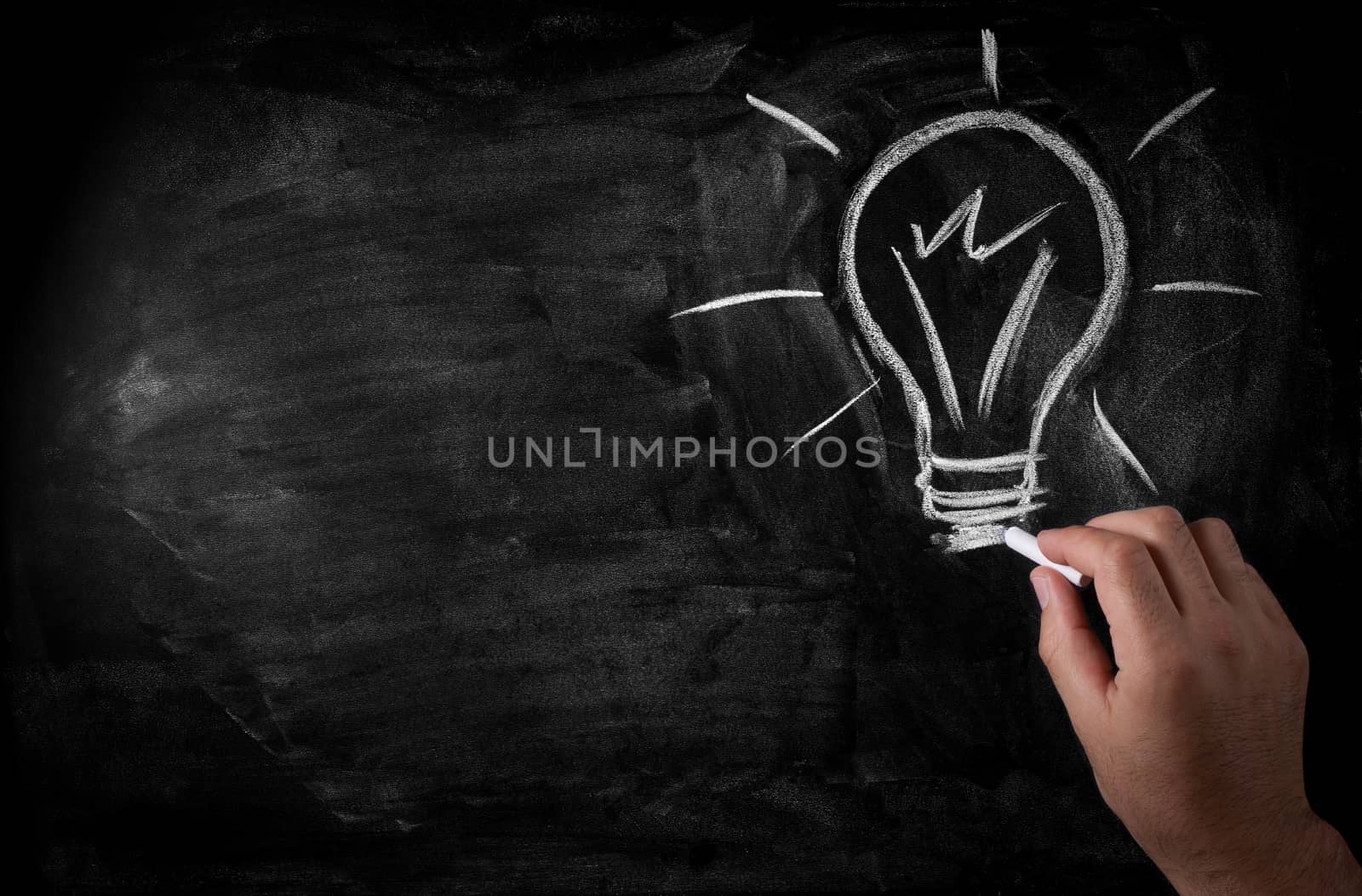 man draws a chalk lightbulb on a black school board
