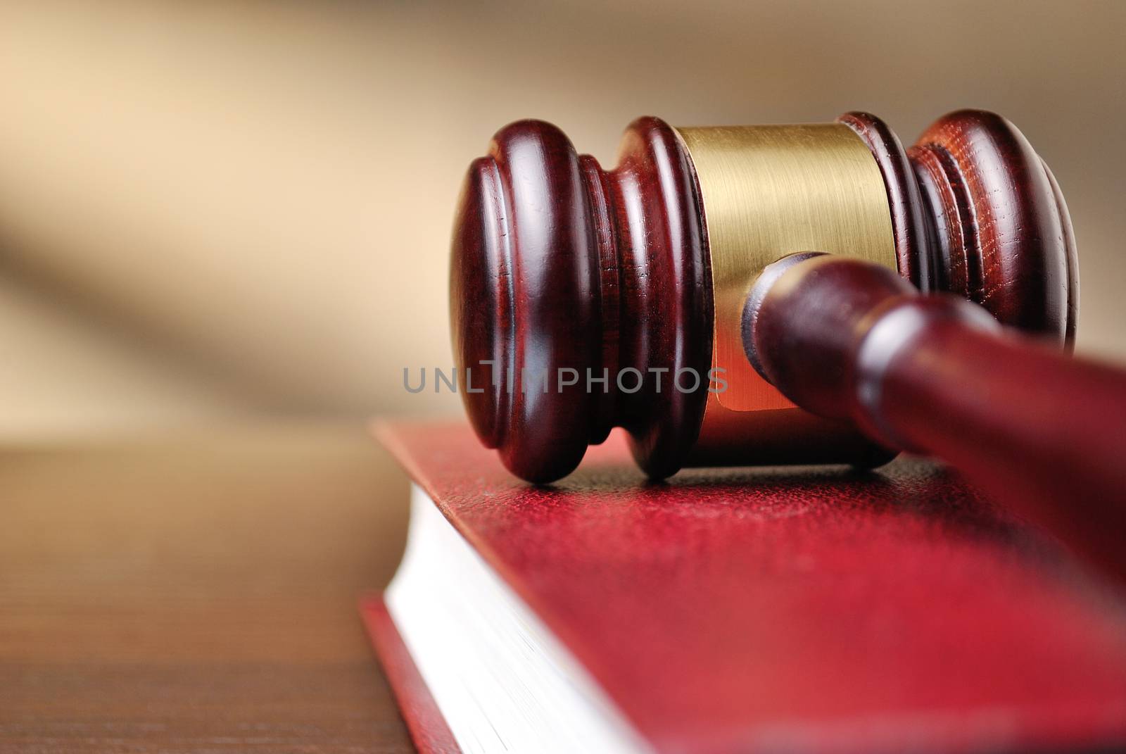 Wooden judges gavel with a brass band around the head resting on top of a closed red law book with shallow dof and copyspace