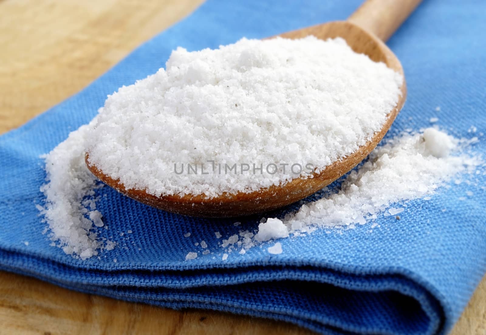 salt in a brown wooden spoon and a blue cloth
